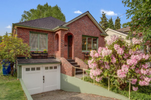 Single family brick house with basement garage in Greenwood neighborhood of Seattle, Washington. House has mature landscape on terraced yard.