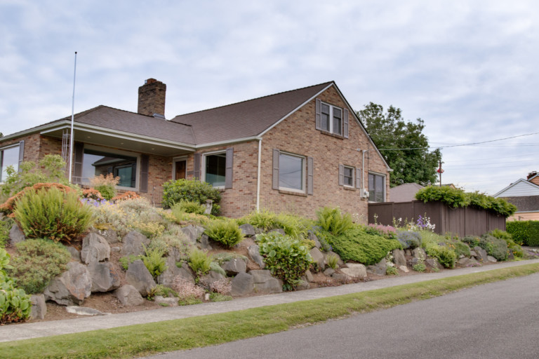 Single family brick exterior home in North Beach Blue Ridge neighborhood of Seattle, Washington. House has mature landscape on terraced yard.