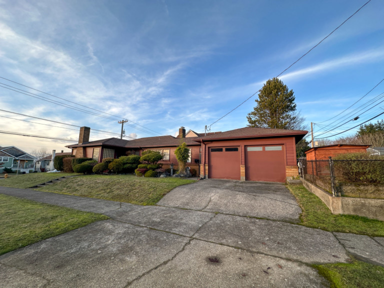 Single family mid-century home in North Beacon Hill neighborhood of Seattle, Washington. House is set back from street with two-car gage with sidewalk in front of house.
