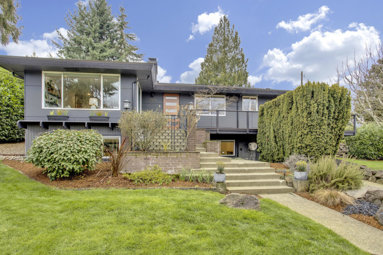 Single family mid-century modern home in Lakeridge neighborhood of Seattle, Washington. House has mature landscape on sloping yard.