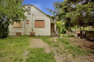 Photo of side yard to house with boarded up windows