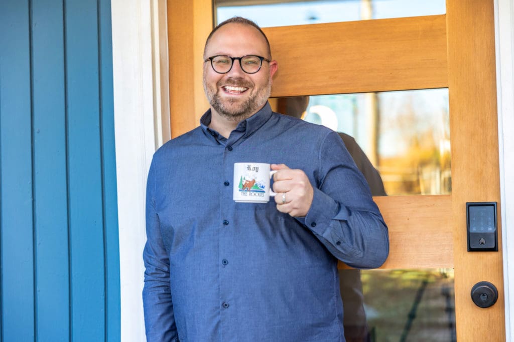 Roy Powell posing in front of a door with a coffee up in his hand