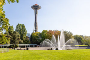 View of Seattle Space Needle with water fountain in the foreground and public park.