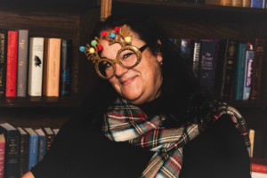 Donna posing in front of a bookshelf wearing reindeer glasses and a plaid scarf